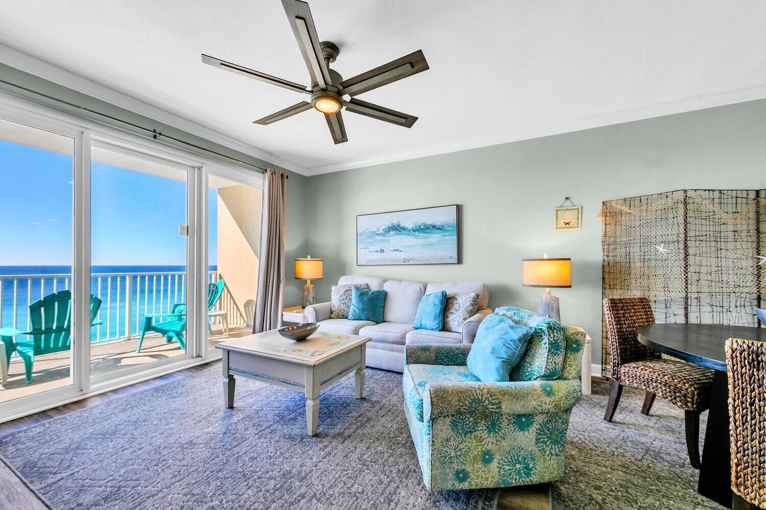 A room with a balcony, a ceiling fan, a sofa, a coffee table, and a dining table with chairs.