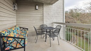 Un balcon doté d’un plancher en bois, d’une table et de chaises en métal, ainsi que d’un canapé aux couleurs vives.