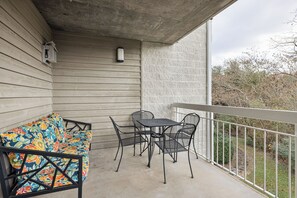 A balcony with a wooden floor, a metal table and chairs, and a colorful sofa.