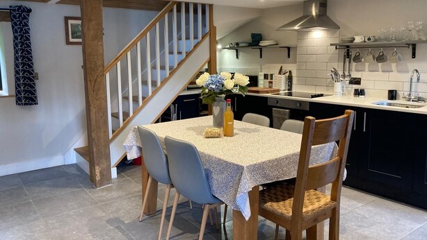 A modern kitchen with a central island, a dining area with a table and chairs, and a staircase leading to an upper level. - Cosy 2 bed barn in Bannau Brycheiniog national park, with outdoor patio.  (Brecon, Powys)