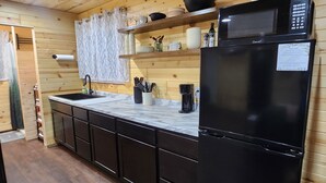 Una cocina moderna con armarios de madera, un refrigerador negro, un microondas y un fregadero.