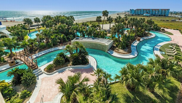 Ein Resort mit großzügigem Poolbereich, Palmen und Blick aufs Meer.
