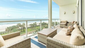 Ein Balkon mit Korbmöbeln, Blick auf das Meer und ein klarer Himmel.