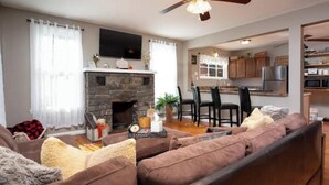 A living room with a stone fireplace, a sofa, and a dining area with chairs. - Cozy Adirondack Escape (Warrensburg)