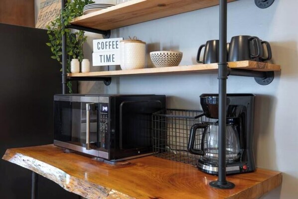 Ett kök med mikrovågsugn, kaffebryggare och en hylla med kaffekoppar samt en skylt med texten ”KAFFEPAUS”.