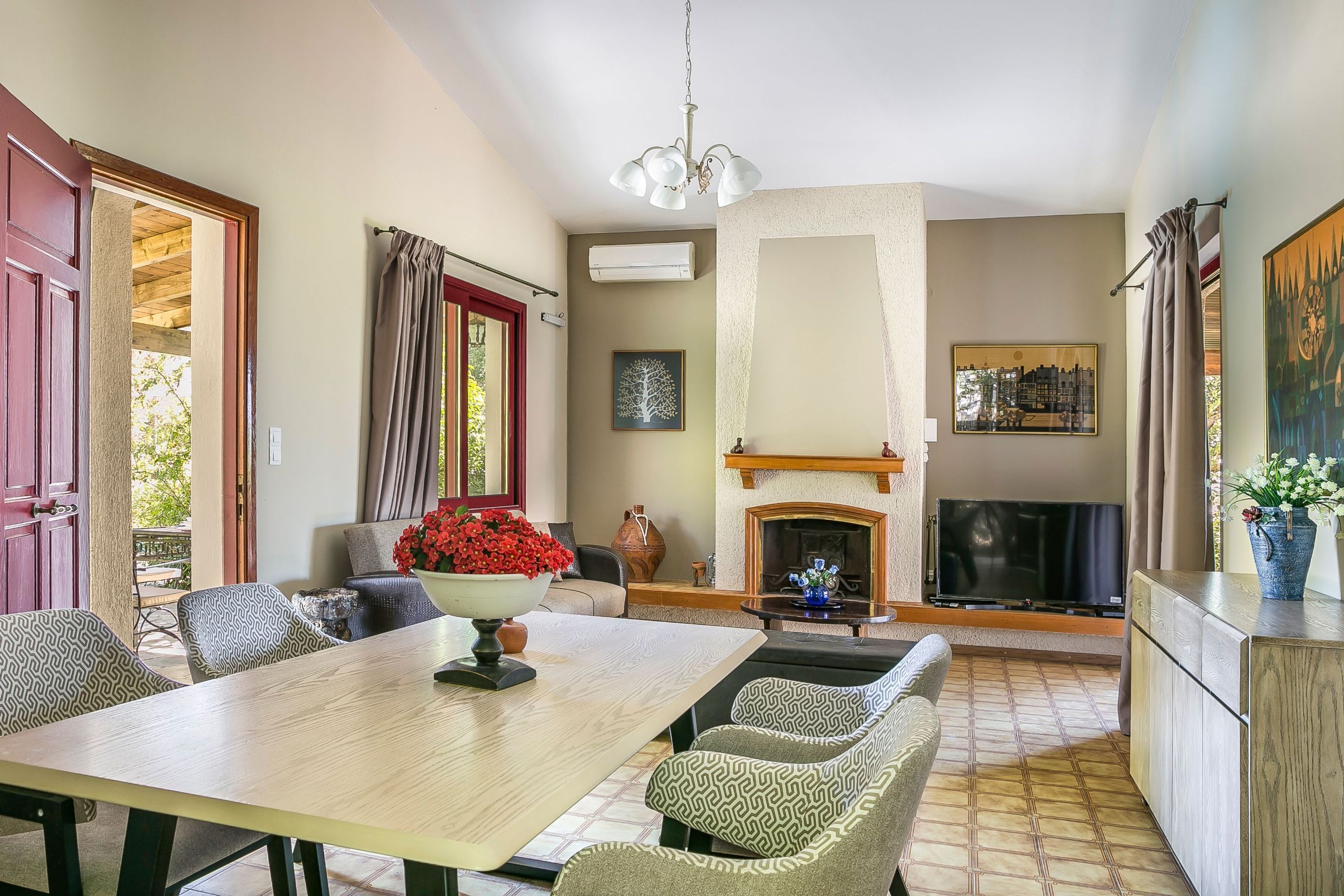 A dining area with a wooden table, patterned chairs, a vase with red flowers, and a fireplace.