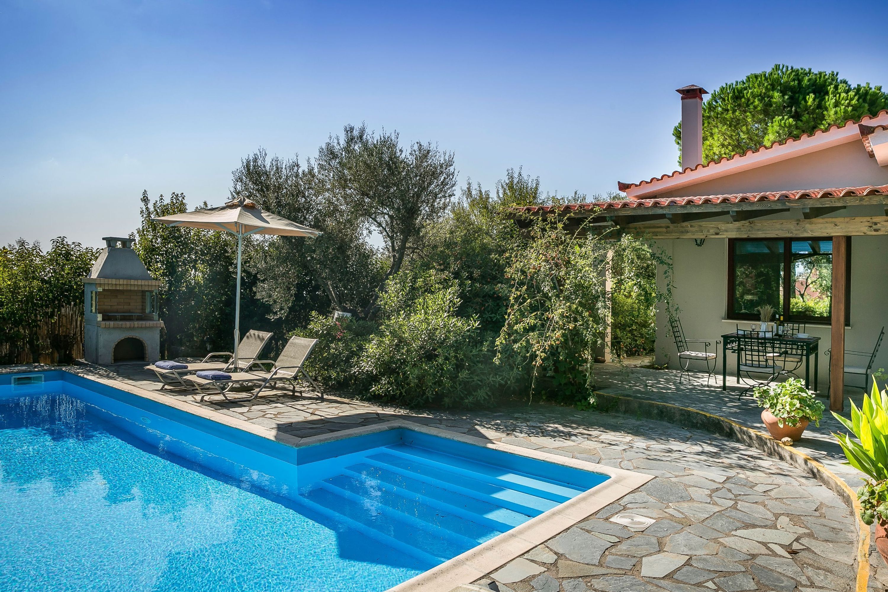 A swimming pool with lounge chairs, a patio area, and a building with a tiled roof.