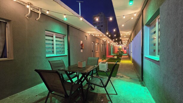 Un étroit couloir extérieur avec une table et des chaises, des guirlandes lumineuses et un extincteur fixé au mur.