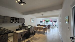 Une cuisine moderne dotée d’un îlot central intégré, un coin repas avec une grande table et des chaises, et une vue à travers la porte vitrée.