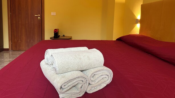 Ein Hotelzimmer mit einem Bett, einer Holztür, einem kleinen Tisch mit einem Heizgerät und einer Wandleuchte.