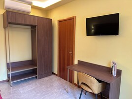 A room with a wardrobe, a desk, a chair, and a flat-screen TV mounted on the wall.