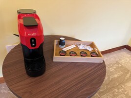 A coffee maker and a tray with coffee pods on a round wooden table.