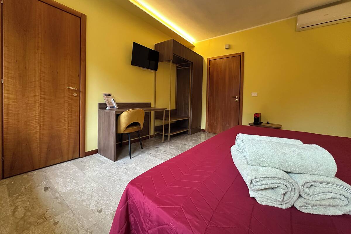 Ein Hotelzimmer mit einem Bett, einem Schreibtisch, einem Sessel und einem an der Wand befestigten Fernseher.