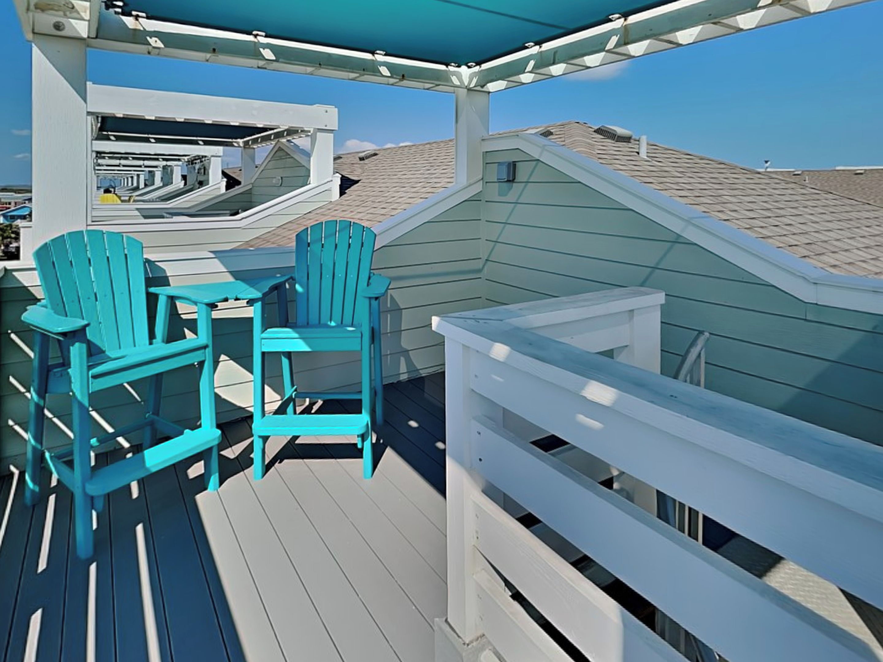 A deck with two turquoise Adirondack chairs and a small table, overlooking a residential area with houses.