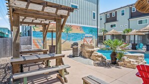 A wooden pergola, a pool with a mural, and a lounge area with chairs. - Port A's Flip Flops & Pop Tops by Silver Sands Vacation Rentals (Port Aransas)