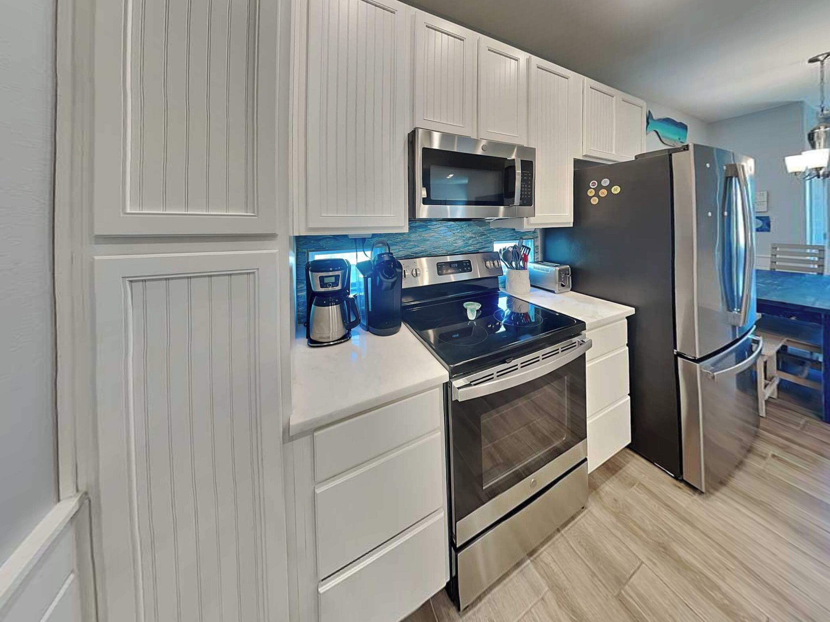 Cocina moderna con armarios blancos, refrigerador de acero inoxidable, microondas, cafetera y tostadora.