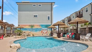 A swimming pool with a mural, lounge chairs, and umbrellas. - Port A's Flip Flops & Pop Tops by Silver Sands Vacation Rentals (Port Aransas)