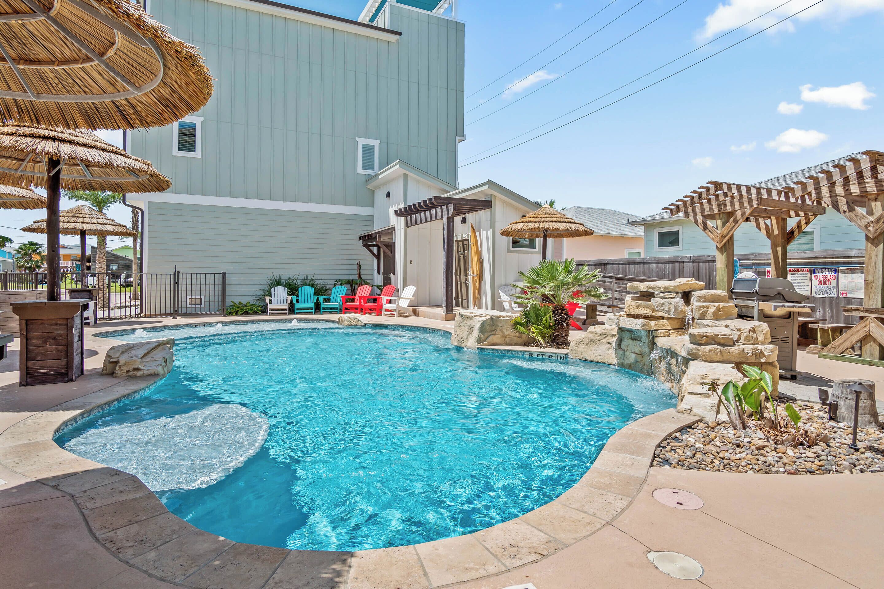 A swimming pool with a stone waterfall feature, surrounded by lounge chairs and umbrellas.