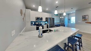 A modern kitchen with white cabinets, stainless steel appliances, a marble island, and pendant lighting. - Port A's Flip Flops & Pop Tops by Silver Sands Vacation Rentals (Port Aransas)