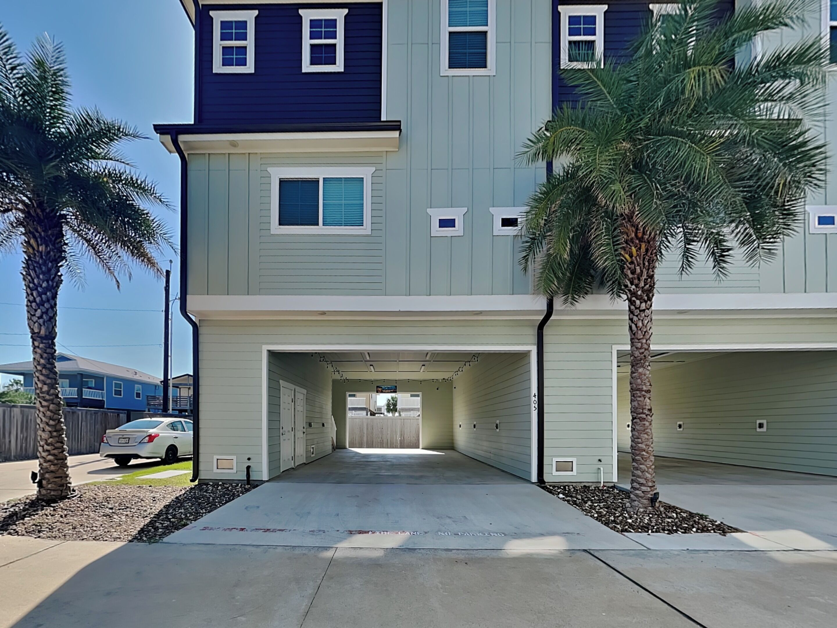 A multi-story residential building with a garage, palm trees, and a clear driveway.