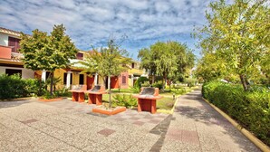 An outdoor courtyard with tiled flooring, outdoor seating, and greenery. - Residence with swimming pool in Ottiolu (Budoni)