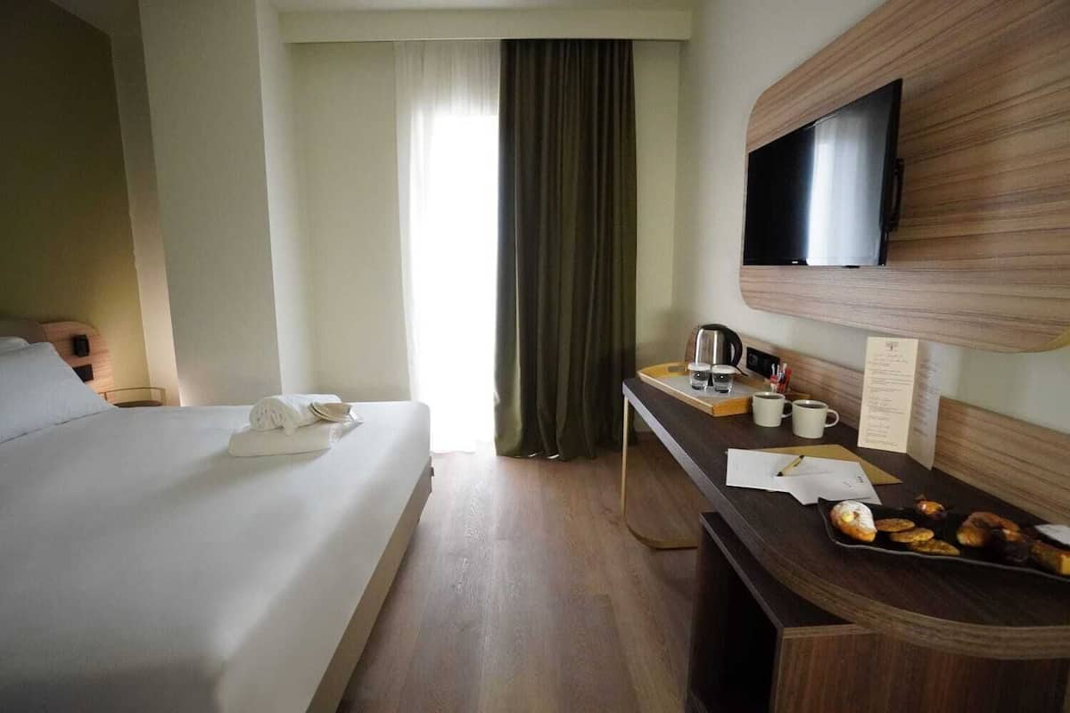 Ein Hotelzimmer mit einem Bett, einem Schreibtisch mit Kaffeemaschine, einem Fernseher und einem Vorhangfenster.