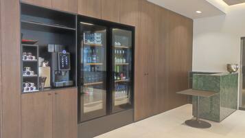 A modern hotel room with wooden paneling, a minibar, and a seating area with a marble table.