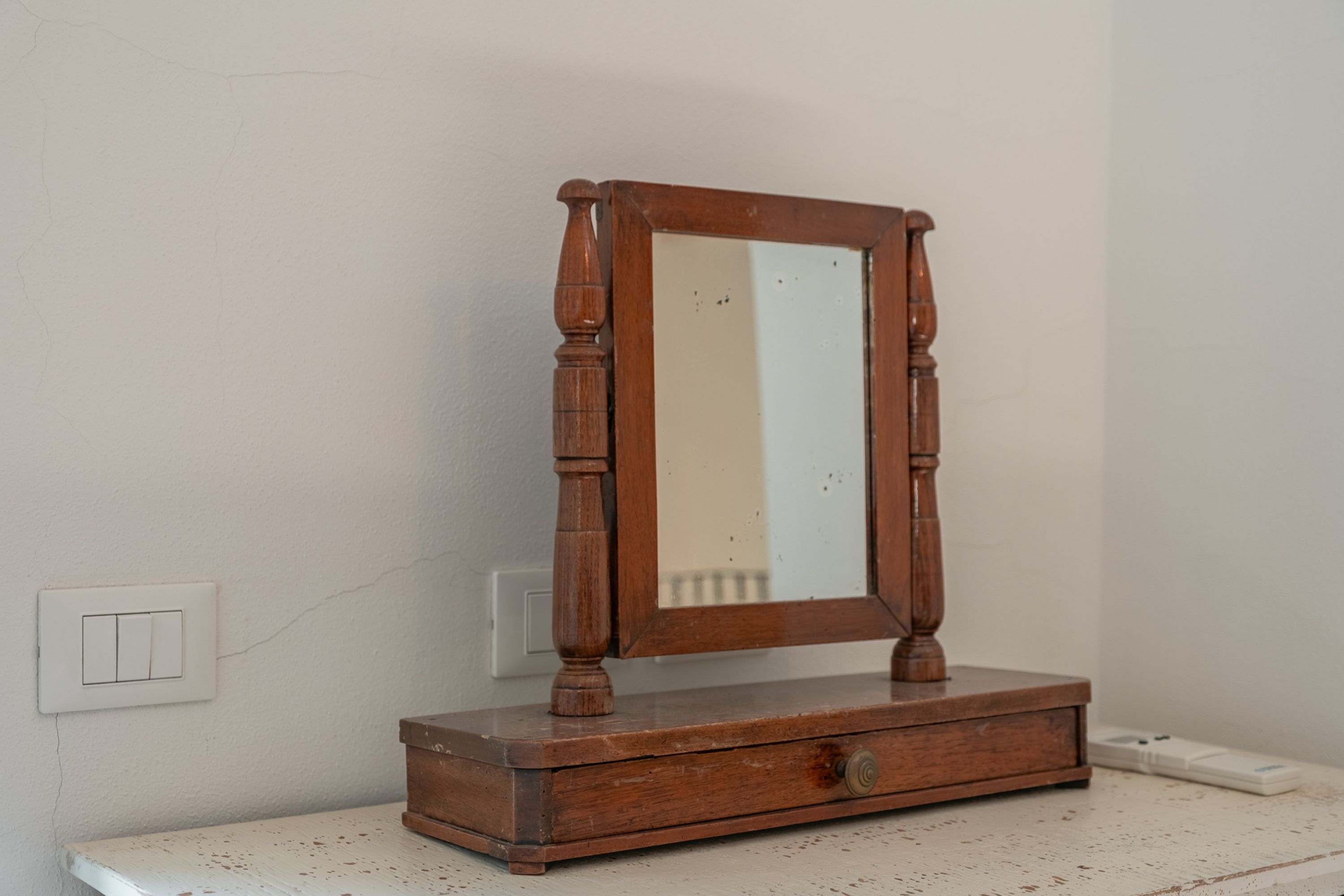 A wooden dresser with a mirror, a drawer, and a switch on the wall.