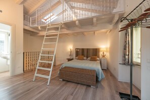 Un dormitorio con una escalera de madera que da a una buhardilla, una cama con colcha azul y un banco de mimbre.
