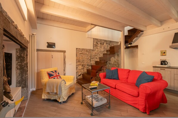 A cozy living room with a red sofa, a yellow armchair with a Union Jack pillow, a small coffee table, and a staircase leading to a kitchen area.
