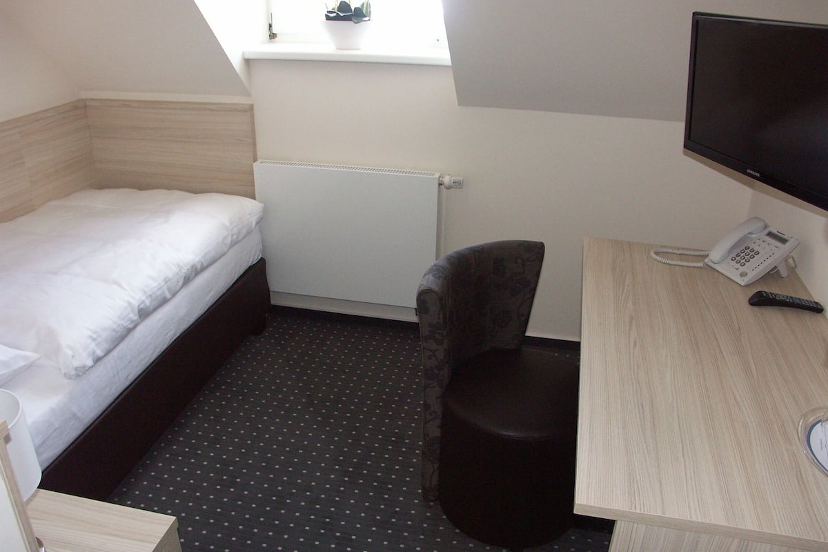 Una habitación de hotel pequeña con una cama individual, un escritorio con teléfono y una silla.