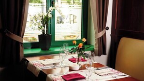 Un tavolo da pranzo apparecchiato con un vaso di fiori, una candela e bicchieri da vino, vicino a una finestra con tende.