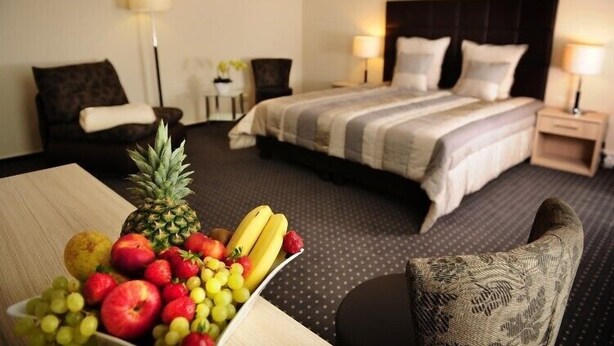 Una camera d'albergo con un letto, due comodini, una sedia e un cesto di frutta su un tavolo.