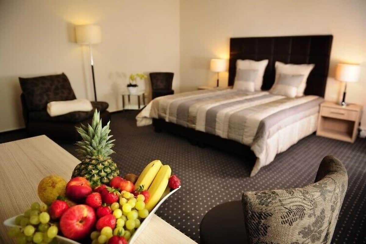 Una habitación de hotel con una cama, dos mesitas de noche, una silla y una cesta de frutas sobre una mesa.