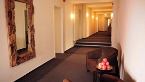 Un corridoio d'albergo con uno specchio con cornice in legno, una poltrona in pelle marrone e un tavolino con delle mele.