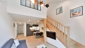 A modern living space with a grey sofa, wooden staircase, and a kitchen in the background.