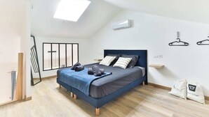 A bedroom with a bed, a skylight, an air conditioning unit, and a wall-mounted hanger.