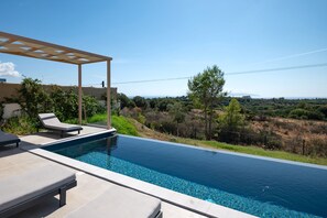 A swimming pool with lounge chairs and a pergola, surrounded by greenery and a view of the landscape. - Villa Ioanna Mentoros (Kefalonia)