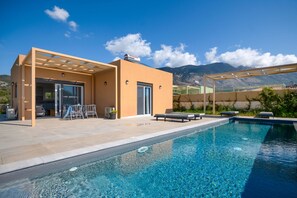 A modern outdoor pool area with a clear view of mountains in the background. - Villa Ioanna Mentoros (Kefalonia)