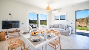 A modern living room with a dining area, large windows, and a view of the outdoors. - Villa Ioanna Mentoros (Kefalonia)