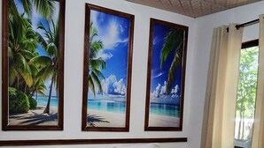 A bedroom with a large bed, a nightstand, and three framed pictures of tropical scenes.