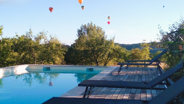 A swimming pool with lounge chairs and hot air balloons in the background. - Le Four à pain, golden triangle Dordogne valley, views garden park swimming pool (saint cybranet)