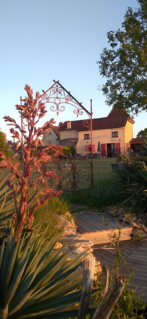 Een huis met een rood pannendak, een tuin met een metalen hek en een geplaveid pad.