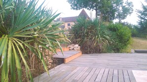 A wooden deck with a stone wall and tropical plants. - Le Four à pain, golden triangle Dordogne valley, views garden park swimming pool (saint cybranet)