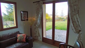 A living room with a brown leather sofa, a framed picture on the wall, and a view of a garden through a glass door. - Le Four à pain, golden triangle Dordogne valley, views garden park swimming pool (saint cybranet)