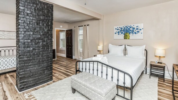 A bedroom with a bed, bedside tables, a wall-mounted artwork, and a brick accent wall. - Stylish Family Retreat | Near Downtown & Street Parking (Pittsburgh)