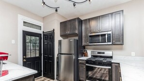 A modern kitchen with stainless steel appliances, dark cabinetry, and a marble countertop. - Stylish Family Retreat | Near Downtown & Street Parking (Pittsburgh)
