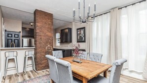 A dining area with a wooden table and grey upholstered chairs, a brick column, and a chandelier. - Stylish Family Retreat | Near Downtown & Street Parking (Pittsburgh)