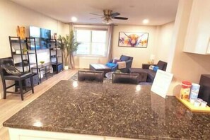 A spacious living area with a large dark granite island, a sofa, and a coffee table. There is a ceiling fan, a window with curtains, and a painting on the wall. - Spacious Downtown Condo Sleeps 4 (Atlanta)