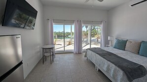 Een slaapkamer met een bed, een plafondventilator, een aan de muur bevestigde televisie en een schuifpui die uitkomt op een buitenruimte.